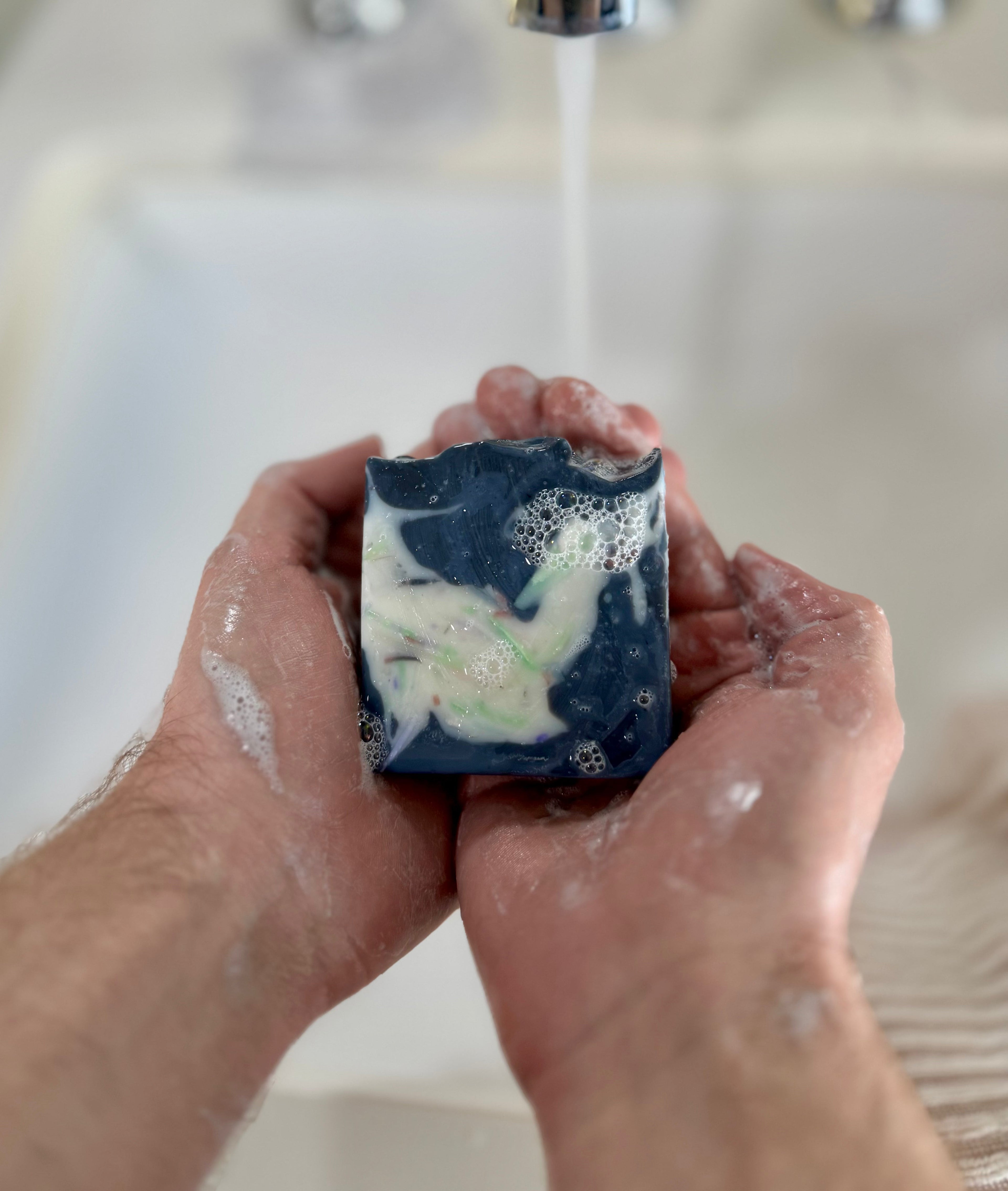 A photo of 5 soaps in a rainbow of colors on a marble background