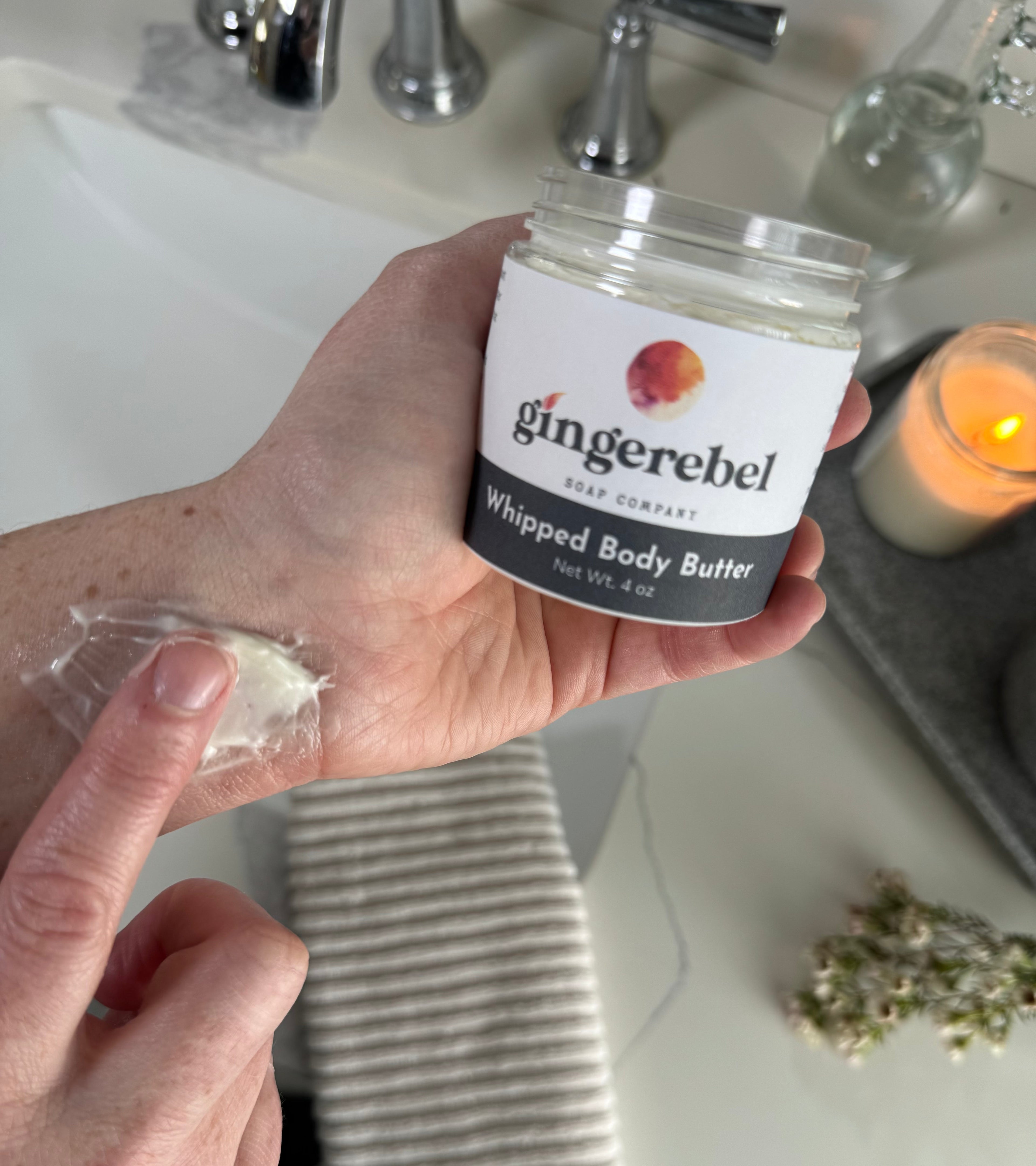 Open jar of whipped body butter being smeared on an arm