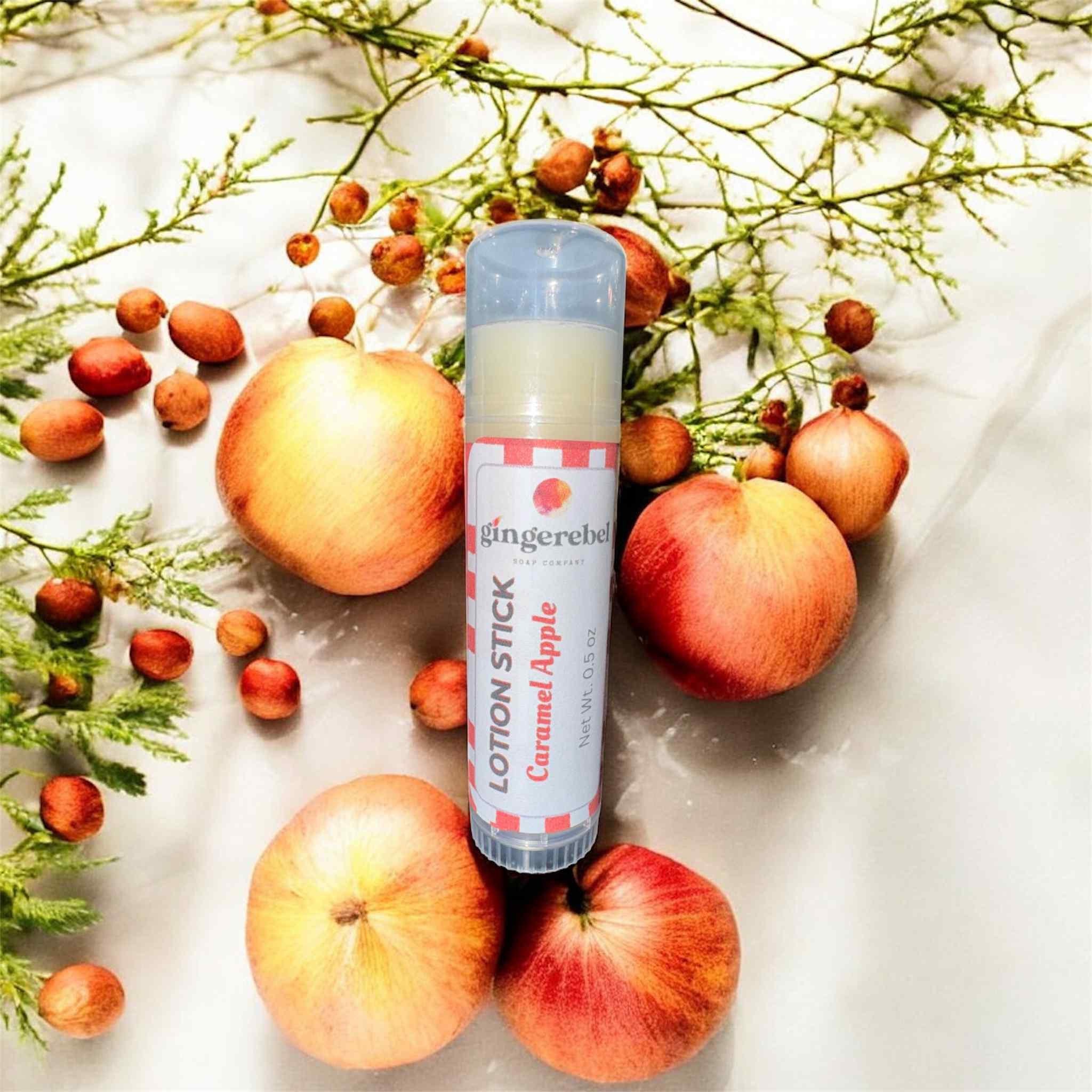 Lotion stick with 'Caramel Apple' scent surrounded by apples and foliage on a light background