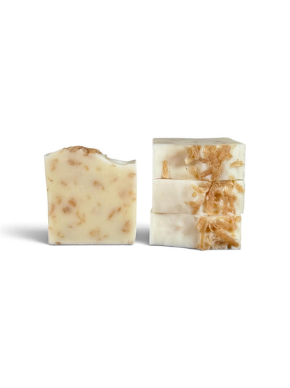 Two bars of handmade soap on a white background, one cut to show the textured cream-colored base with tan botanical inclusions, and one stacked showing the cross-section with the same pattern.