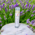 Lotion stick with lavender and sage label on a marble surface surrounded by lavender flowers