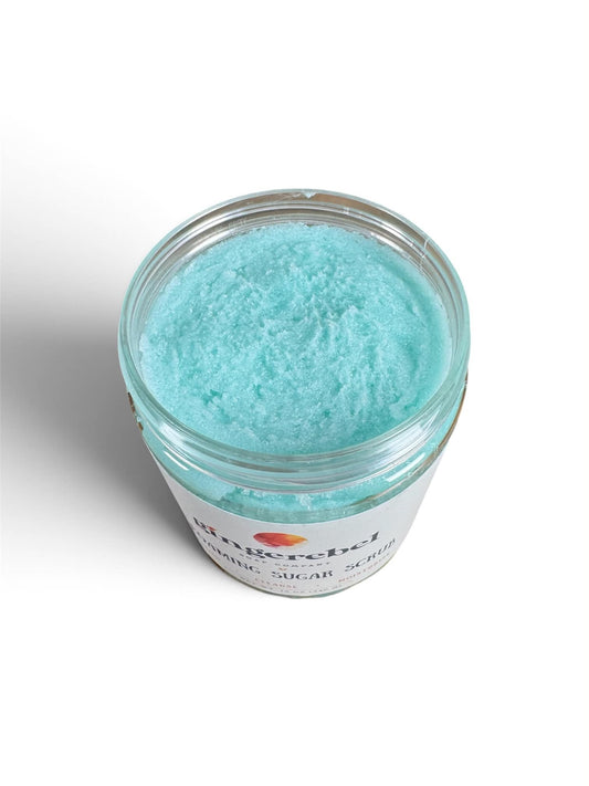 An open clear jar of light blue cosmetic sugar scrub with a white label, photographed on a clean white background.
