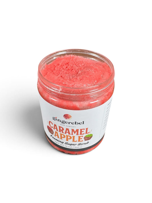 A jar of gingerebel Caramel Apple exfoliating sugar scrub, showing the pinkish-red scrub through a clear lid, on a white background.