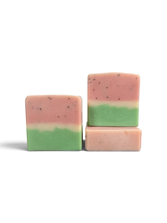 Three rectangular layered soap bars with a pink top half, light green bottom half, and small dark specks, arranged on a plain white background.