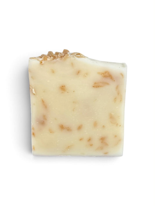A rectangular bar of creamy off-white soap with small tan botanical inclusions and a rough, textured cut edge, shown on a plain white background.
