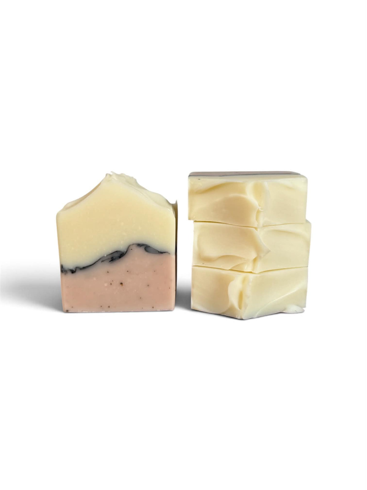 Two handmade soap bars on a white background, one cut to show a two-tone cream and dusty pink layer with a dark marbled line, and one stacked bar in solid cream.