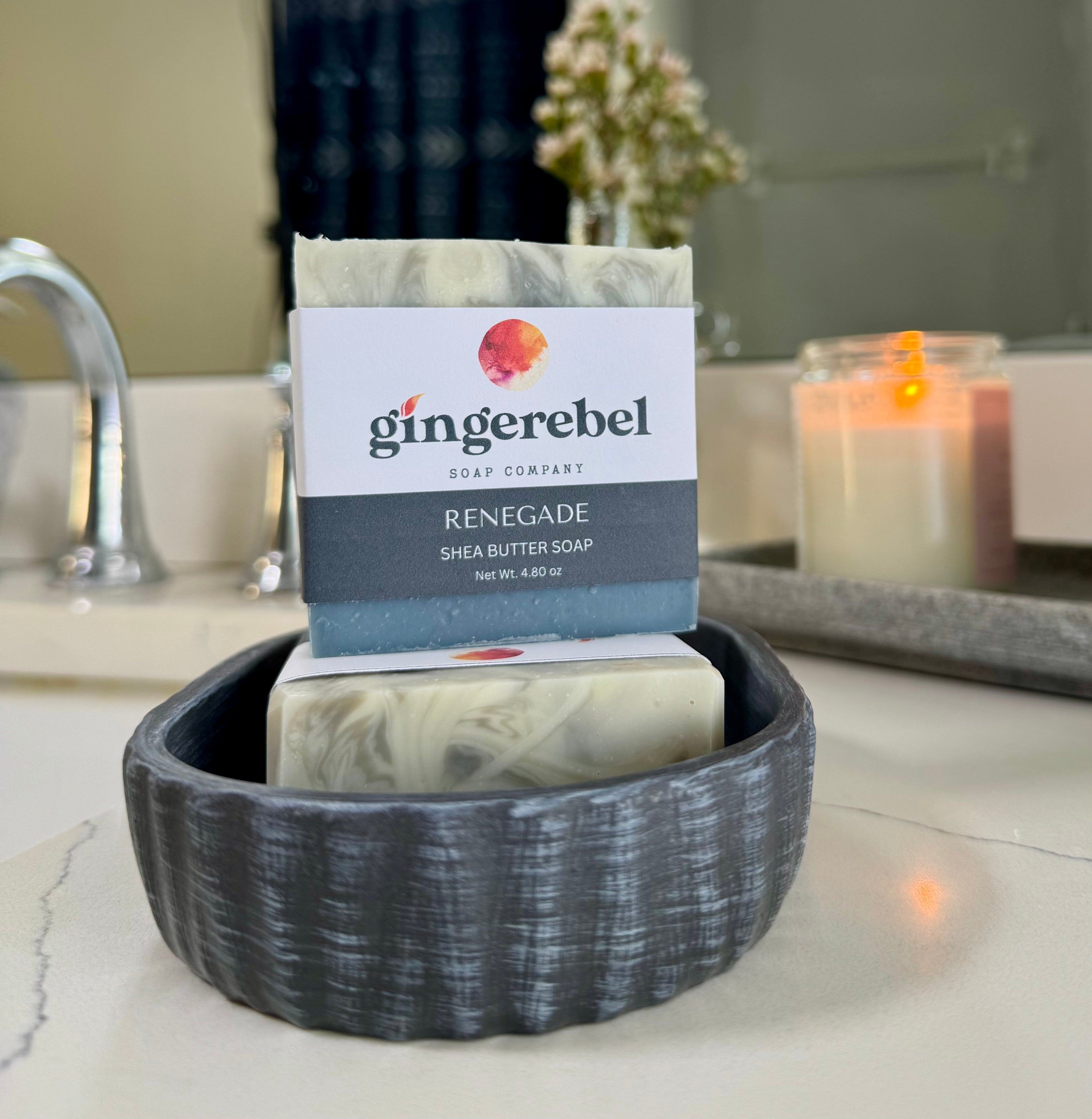 Gingerebel soap in a black soap dish on a bathroom counter with a candle in the background.