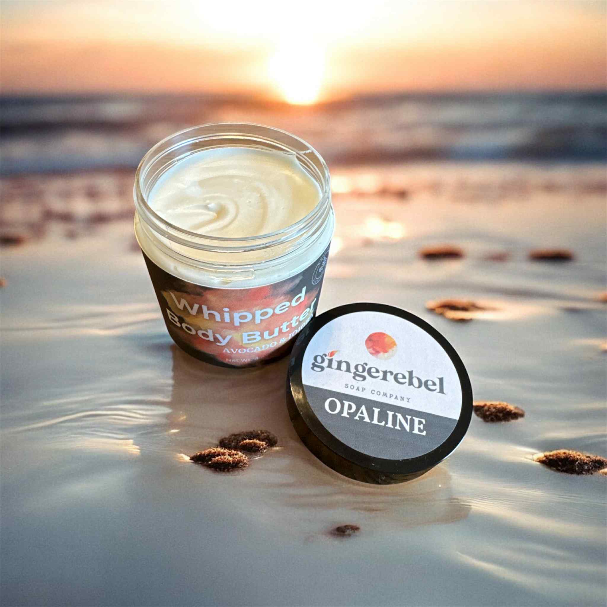 an opened jar of white opaline whipped body butter with a beach background. 