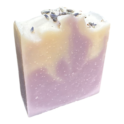A bar soap with a gradient from white to purple, topped with lavender flowers on a white background.