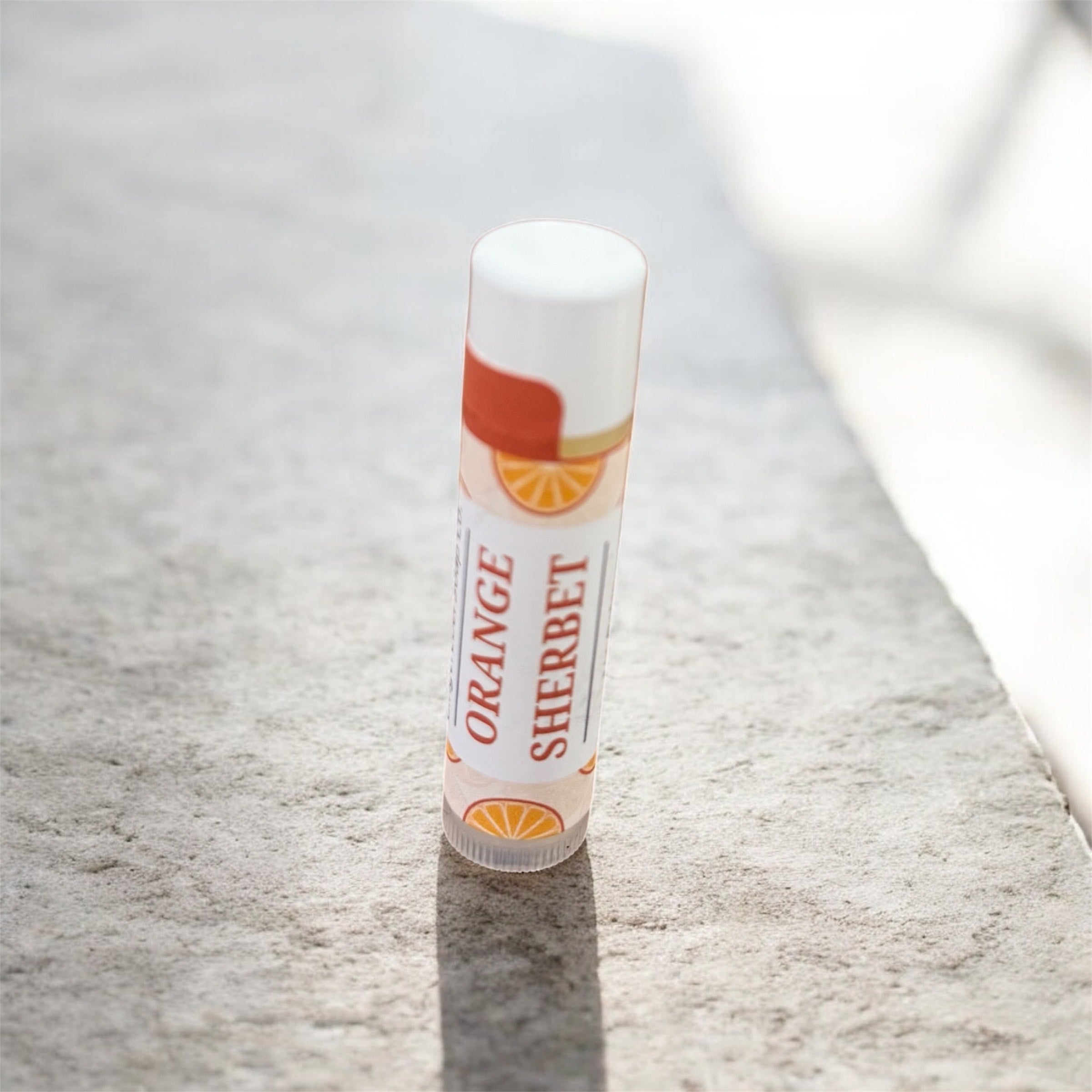 Lip balm labeled 'Orange Sherbet' on a textured surface