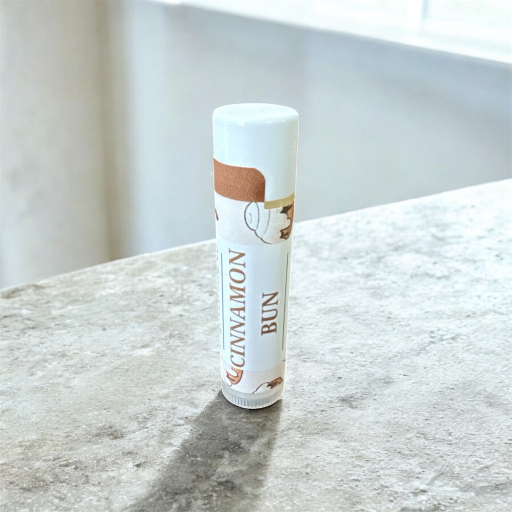 Lip balm tube labeled 'Cinnamon Bun' on a marble surface