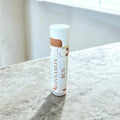 Lip balm tube labeled 'Cinnamon Bun' on a marble surface
