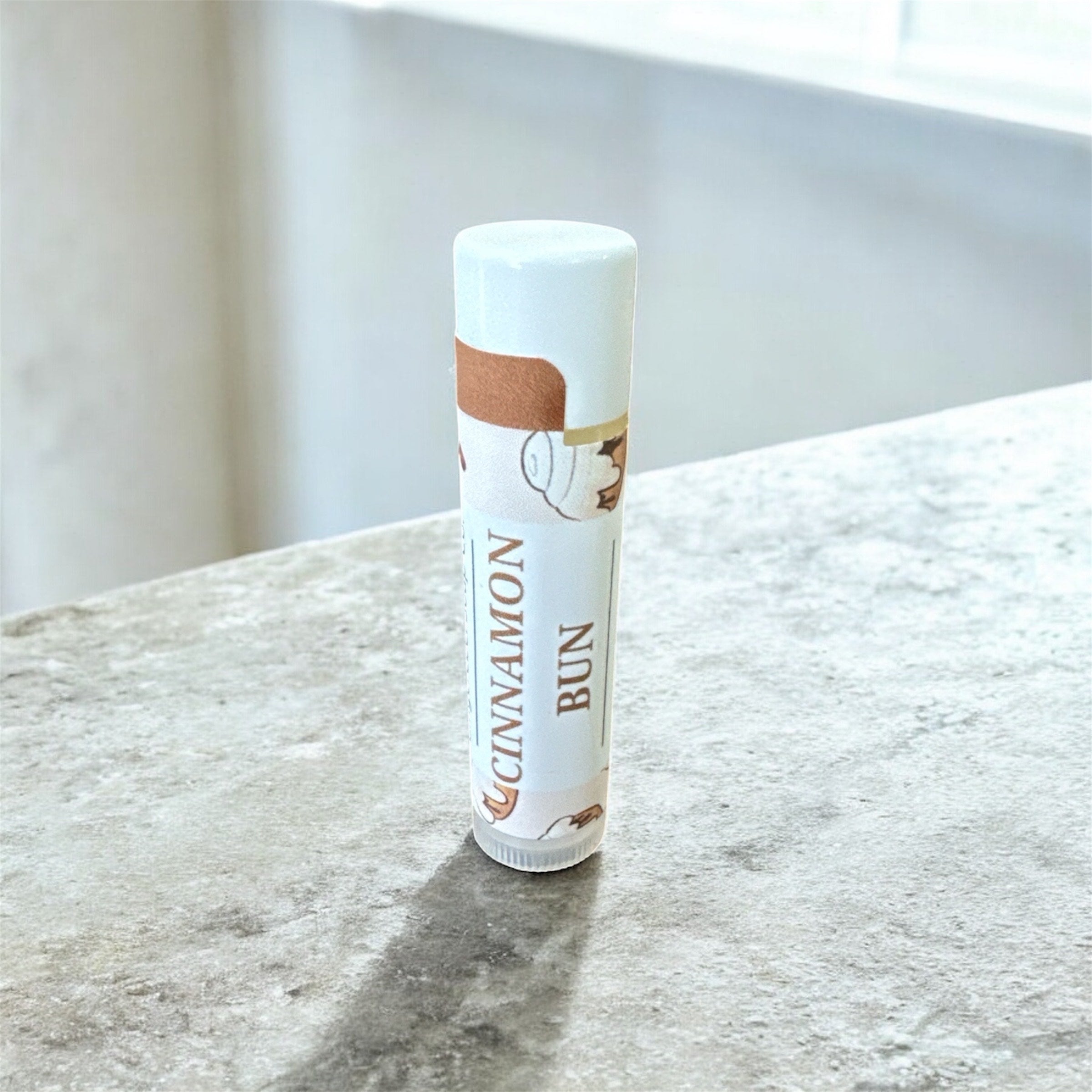 Lip balm tube labeled 'Cinnamon Bun' on a marble surface