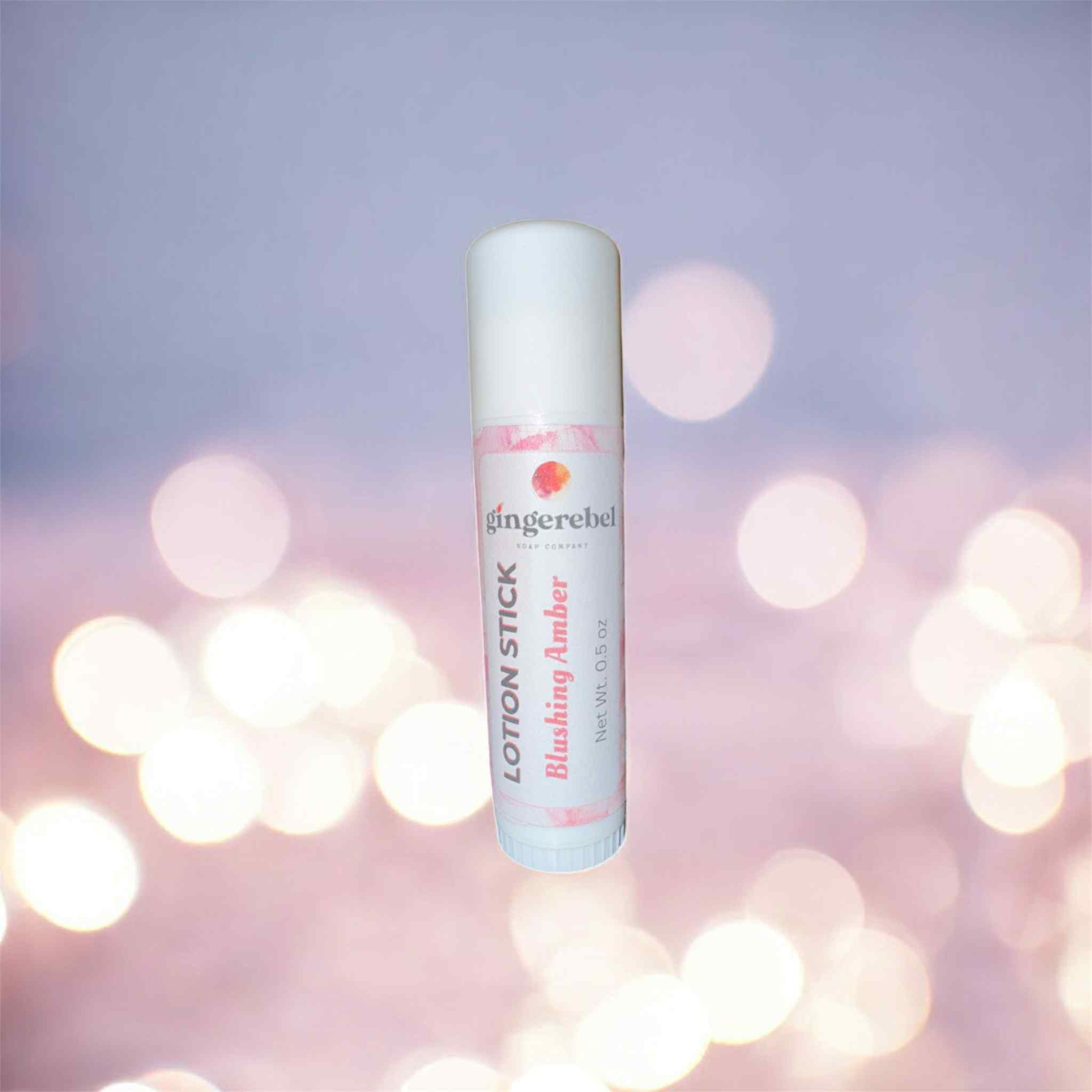 Lotion stick scented in blushing amber with gingerebel branding on a blurred lights background