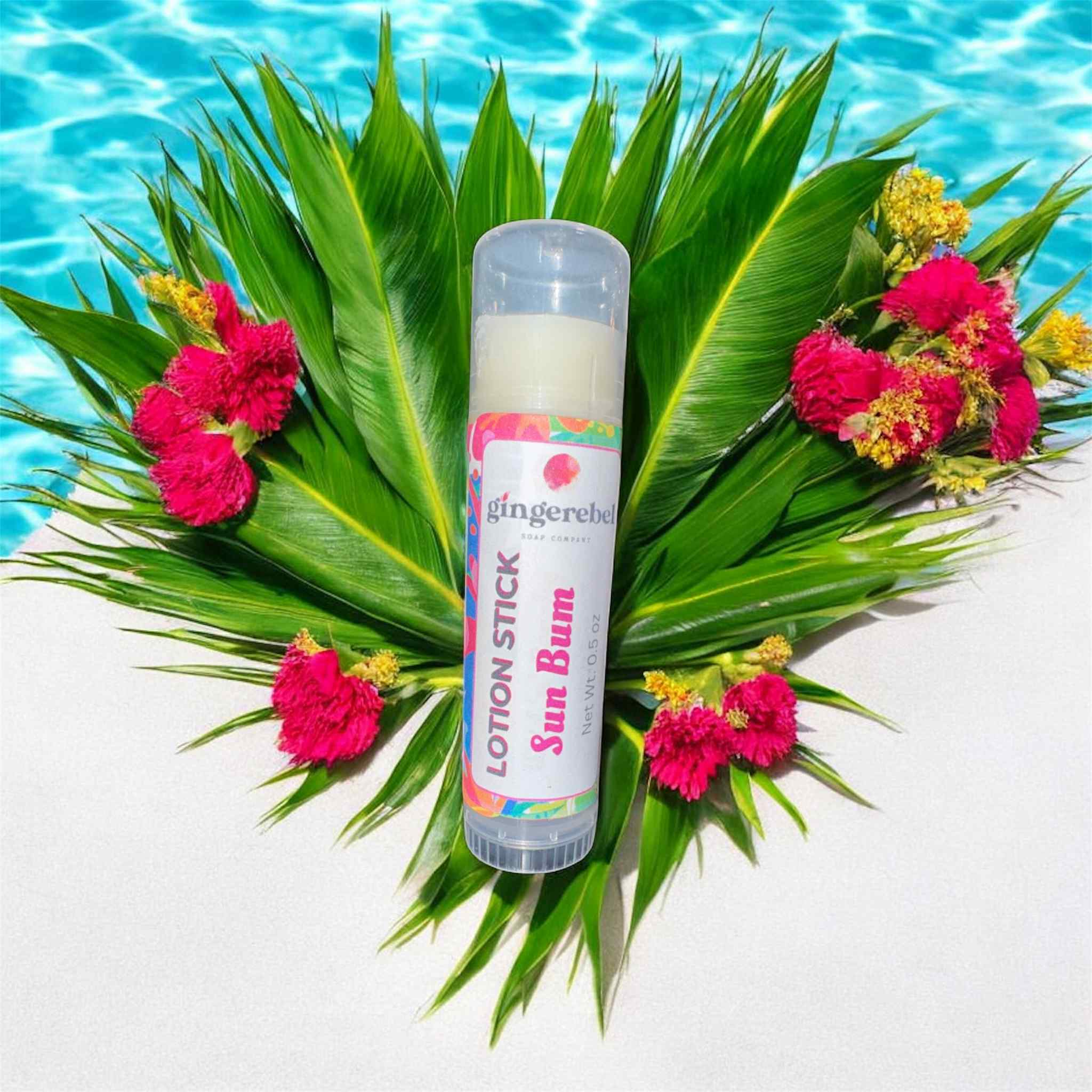 Lotion stick in sun bum scent on a leafy arrangement with flowers by a pool