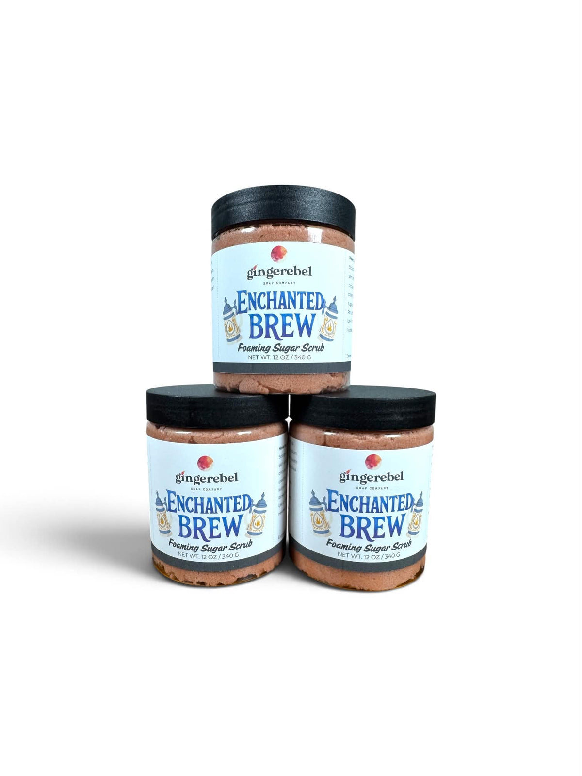 Three glass jars of gingerebel Enchanted Brew Footing Sugar Scrub stacked in a pyramid arrangement on a white background.