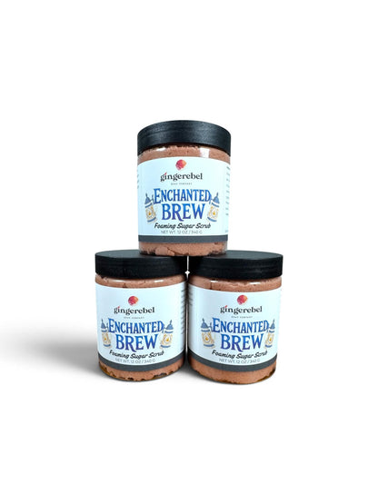 Three glass jars of gingerebel Enchanted Brew Footing Sugar Scrub stacked in a pyramid arrangement on a white background.